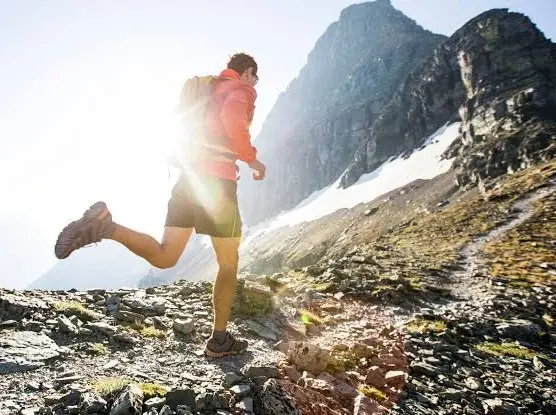 Trail runner on a rocky alpine trail below a mountain peak